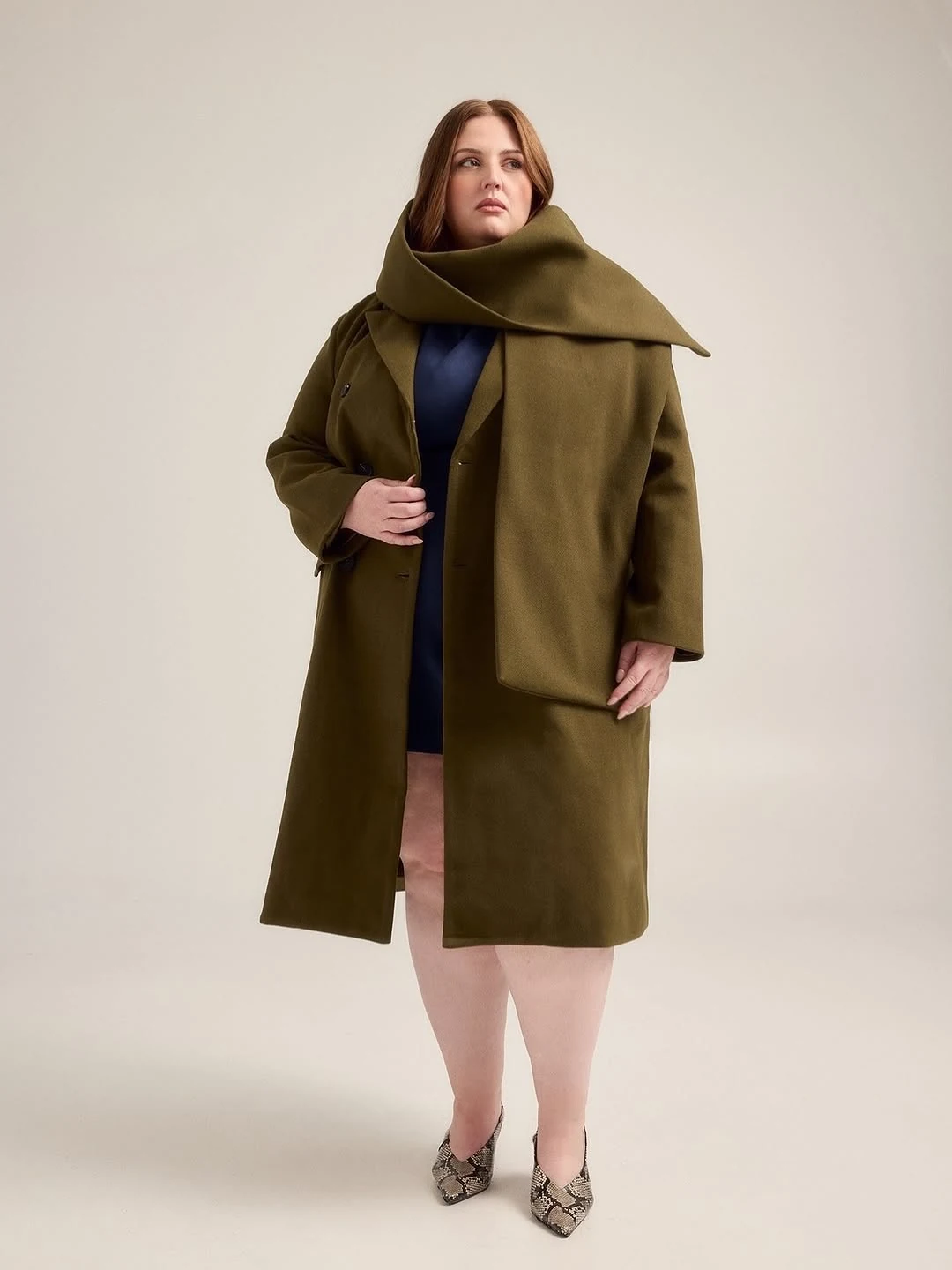An Olive Funnel-Collar Coat Over a Navy Dress on a petite woman
